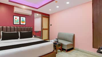 A hotel room with a bed, a chair, a small table with a kettle, and a wall-mounted air conditioner.