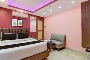 Habitación de hotel con cama, una silla, una mesita con tetera y aire acondicionado de pared.