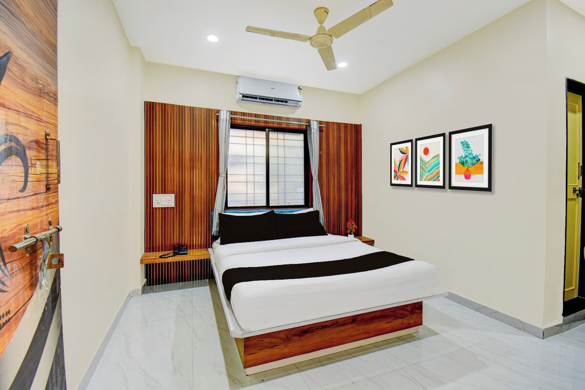 A bedroom with a bed, a ceiling fan, an air conditioning unit, a window with curtains, and framed artwork on the wall.