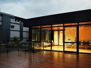 A modern building with large glass windows, a wooden deck, and a seating area with chairs and a table.