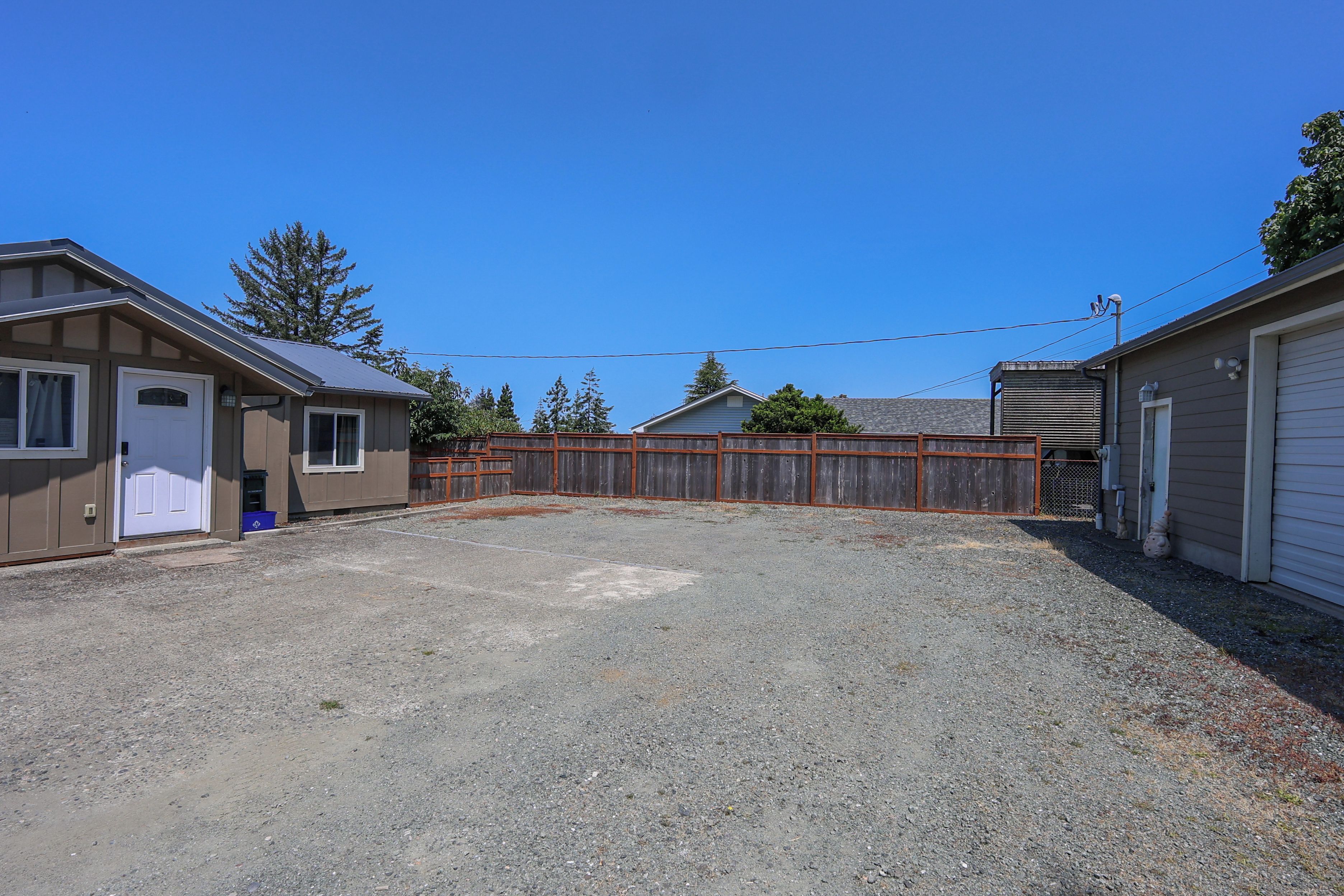 A residential area with a gravel driveway, wooden fences, and houses with garage doors.