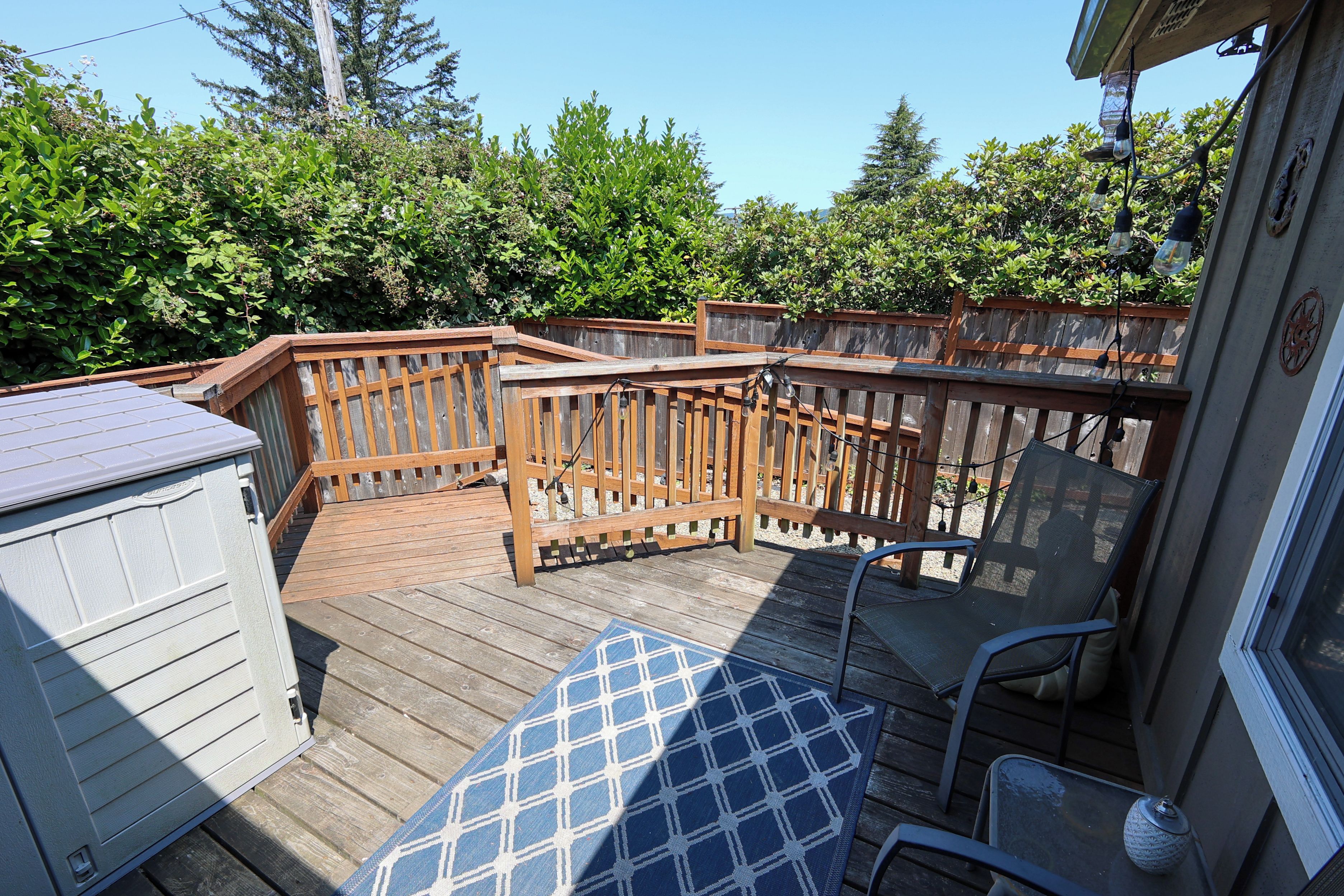 A wooden deck with a blue patterned rug, a metal chair, and a wooden fence.