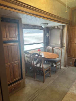 A dining area with a wooden table and chairs, a window with blinds, and a wall-mounted lamp. - Charming RV Stay on a Working Farm-Ultimate Country Escape! (Cottondale)