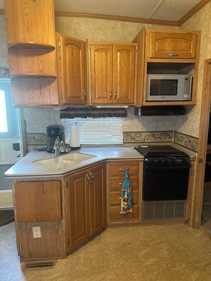A compact RV kitchen with wooden cabinets, a microwave, a stove, and a sink. - Charming RV Stay on a Working Farm-Ultimate Country Escape! (Cottondale)