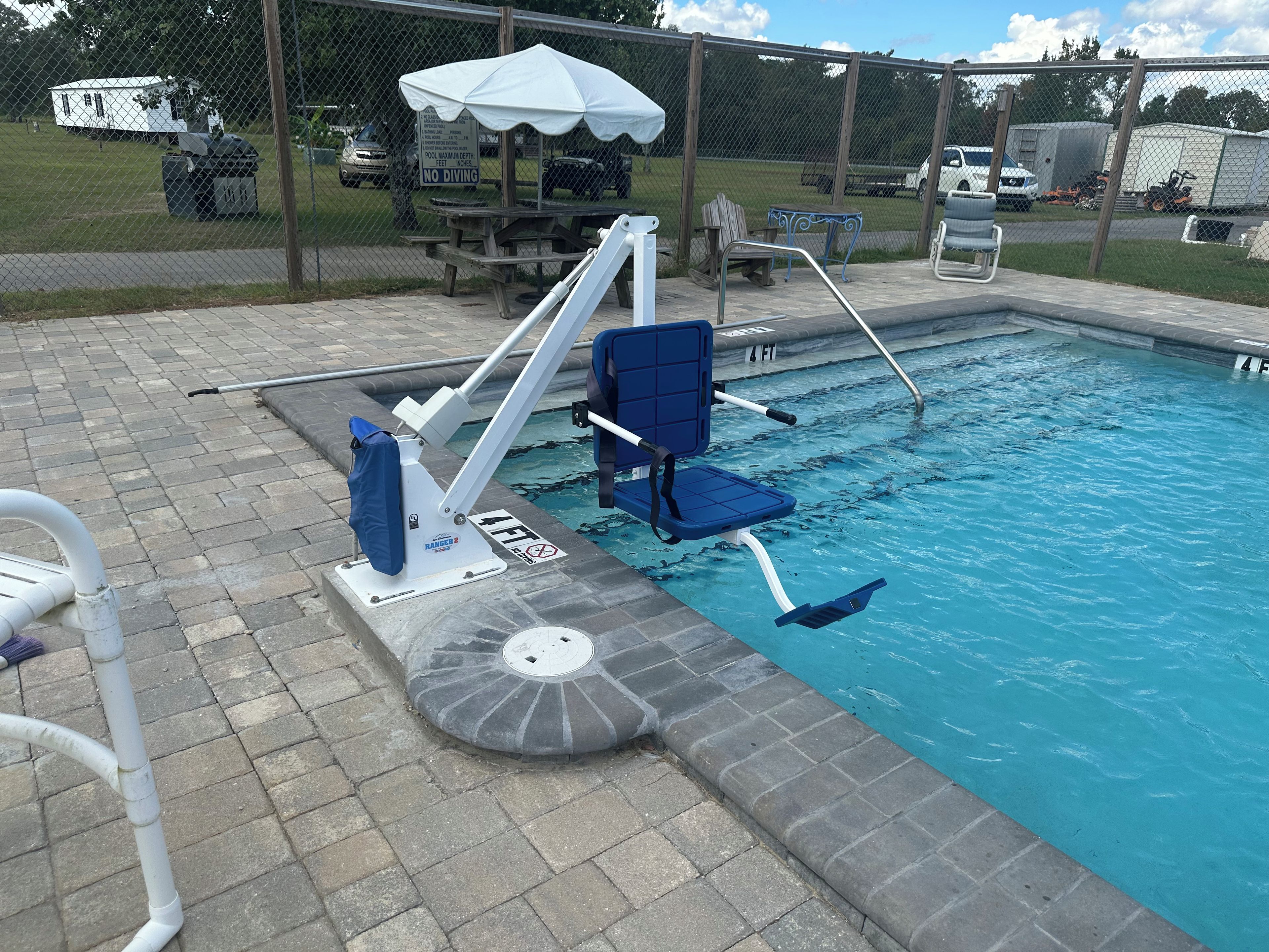 Une piscine avec un plongeoir, un banc et une table de pique-nique couverte.