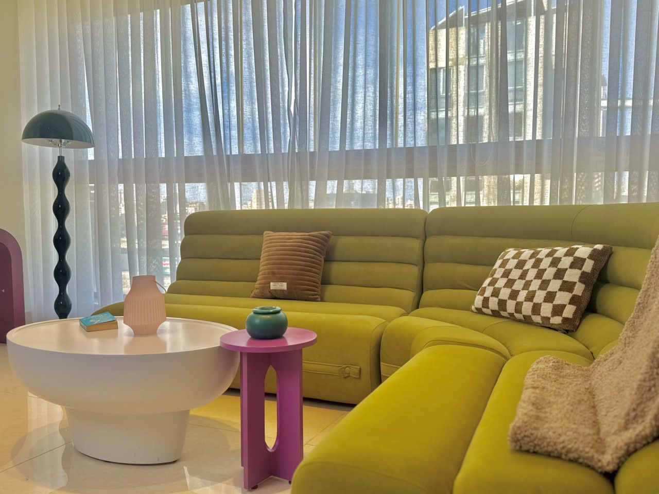 A modern living room with a green sofa, a white coffee table, and a small pink side table.