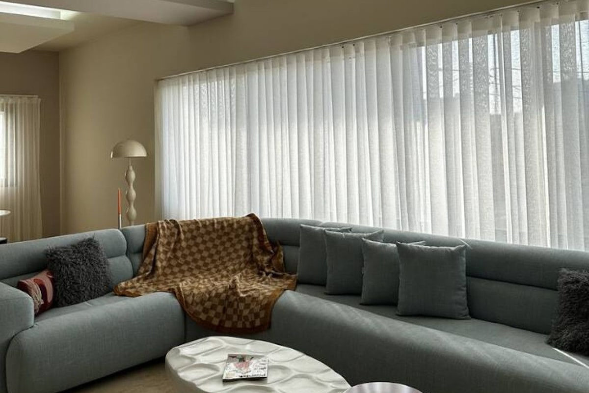 A modern living room with a sectional sofa, a coffee table, and a large window with sheer curtains.