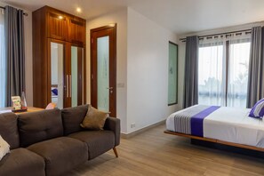 A modern hotel room with a sofa, a bed with a striped bedspread, a wooden wardrobe, and a large window with curtains. - Garden suite 301 (Adenta Municipality)