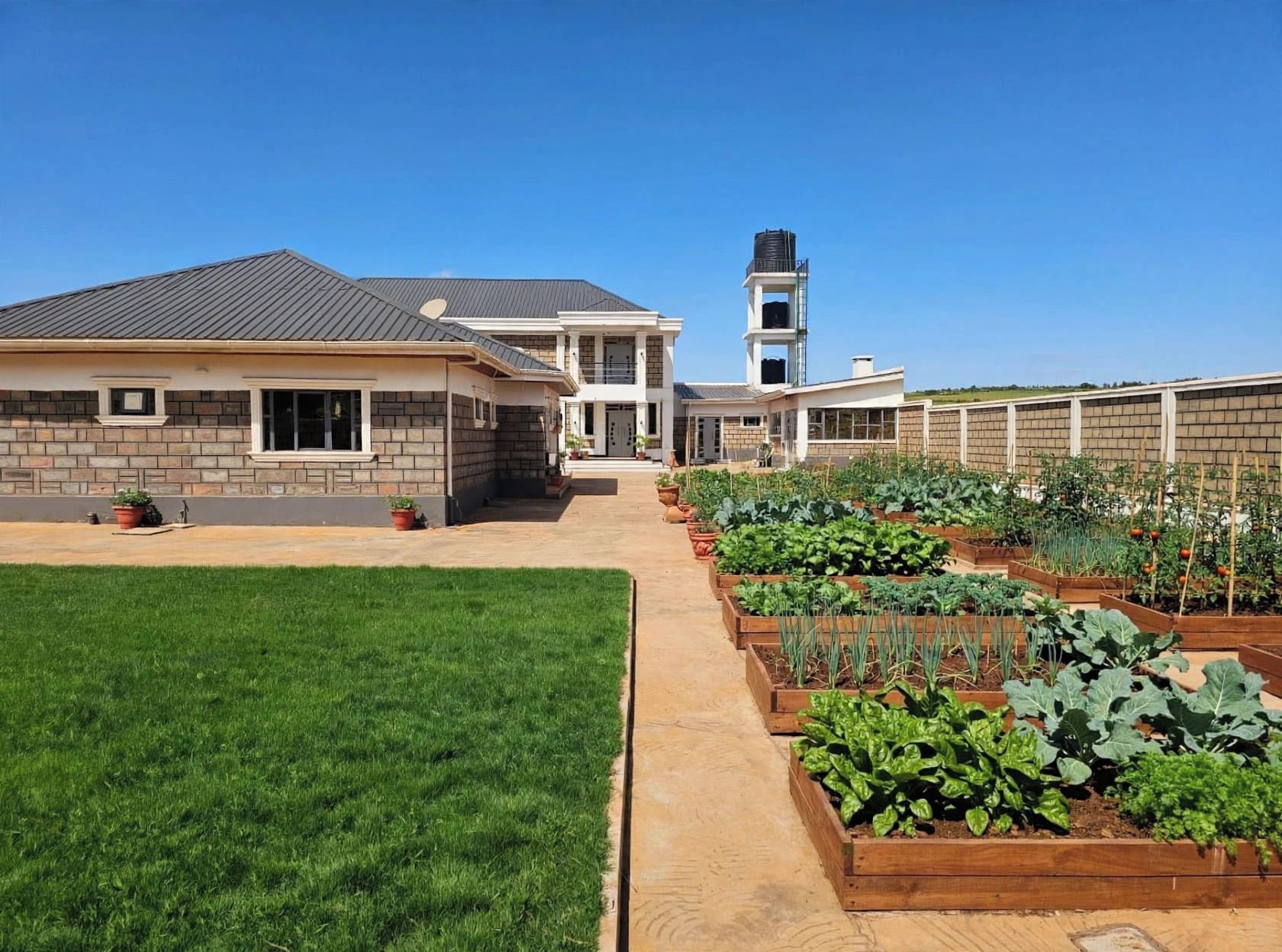 Il s'agit d'une propriété résidentielle dotée d'une pelouse bien entretenue, d'un jardin avec des plates-bandes surélevées et d'une maison à deux étages surmontée d'un château d'eau.