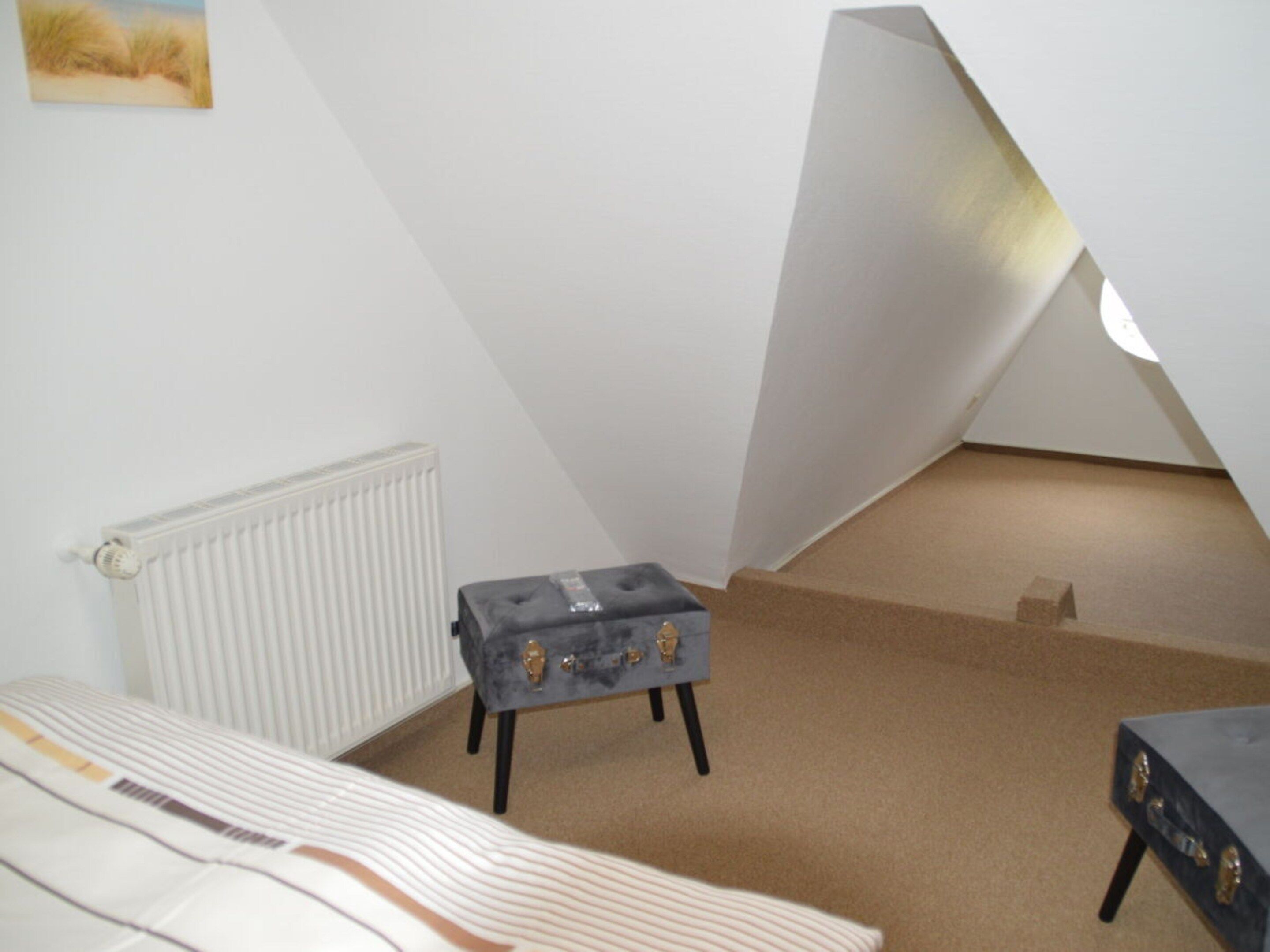 A room with a bed, a small table, a radiator, and a sloped ceiling.