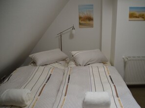 A bedroom with a bed, pillows, a bedside lamp, and two wall art pieces. - Hus am a Suud Ferienwohnung Ley (Dunsum)
