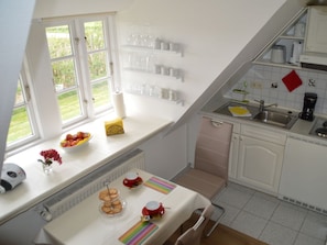 A kitchen with a window, a table with a tray of cookies, and a red cup on the windowsill. - Hus am a Suud Ferienwohnung Ley (Dunsum)