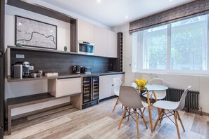 Et moderne køkken med indbyggede hårde hvidevarer, et spiseområde med et bord og stole samt et stort vindue der giver naturligt lys.