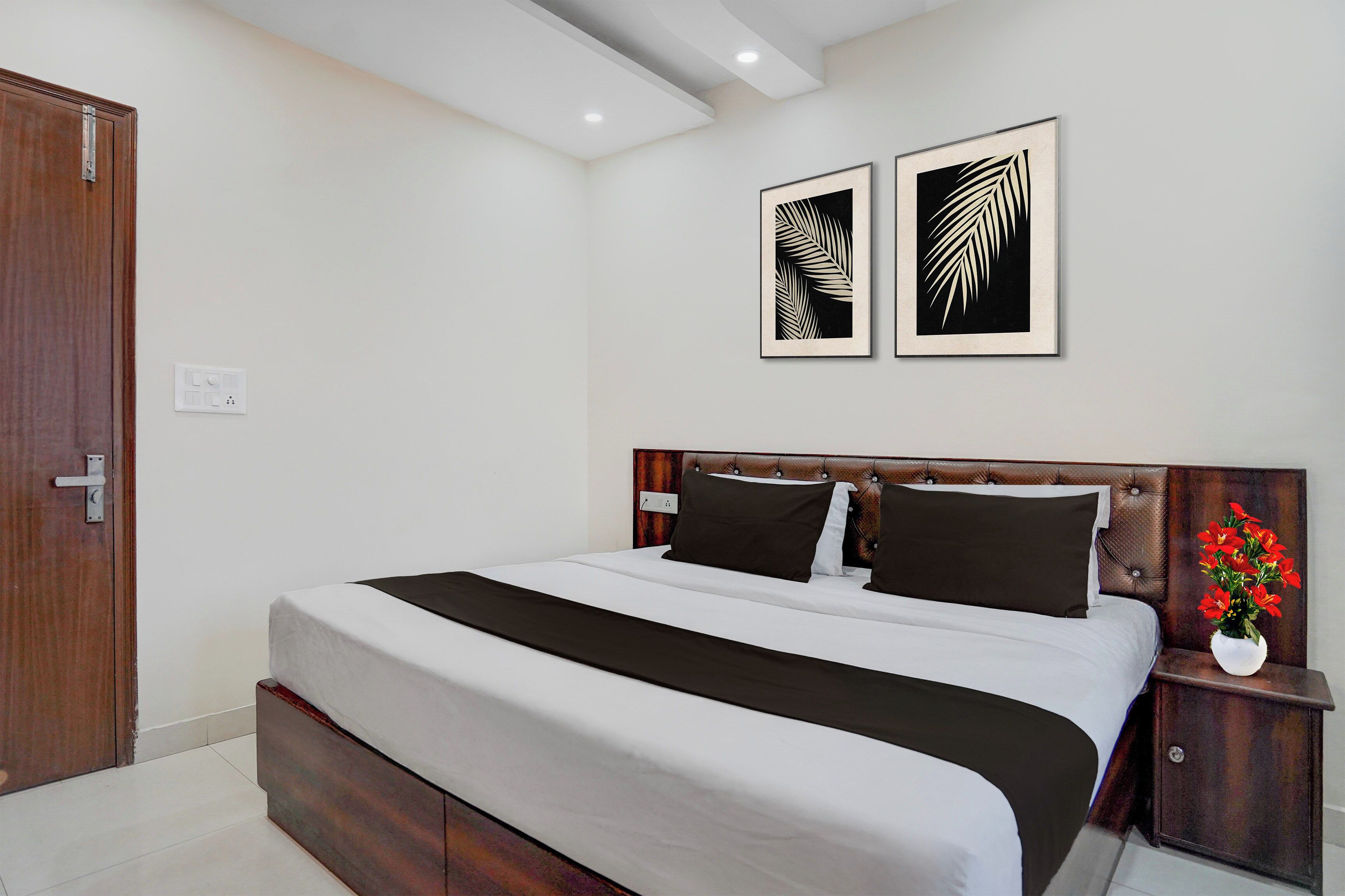 Een slaapkamer met een bed, een nachtkastje, een vaas met bloemen en twee ingelijste foto's aan de muur.