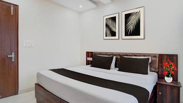 Un dormitorio con cama, mesita de noche, un florero con flores y dos cuadros en la pared.