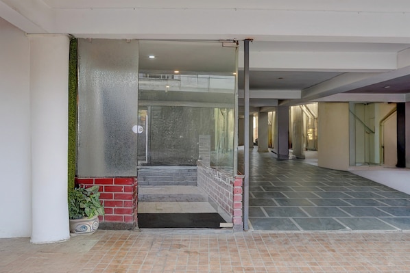Corredor com porta de vidro que dá para uma escadaria, um vaso de planta e piso ladrilhado.