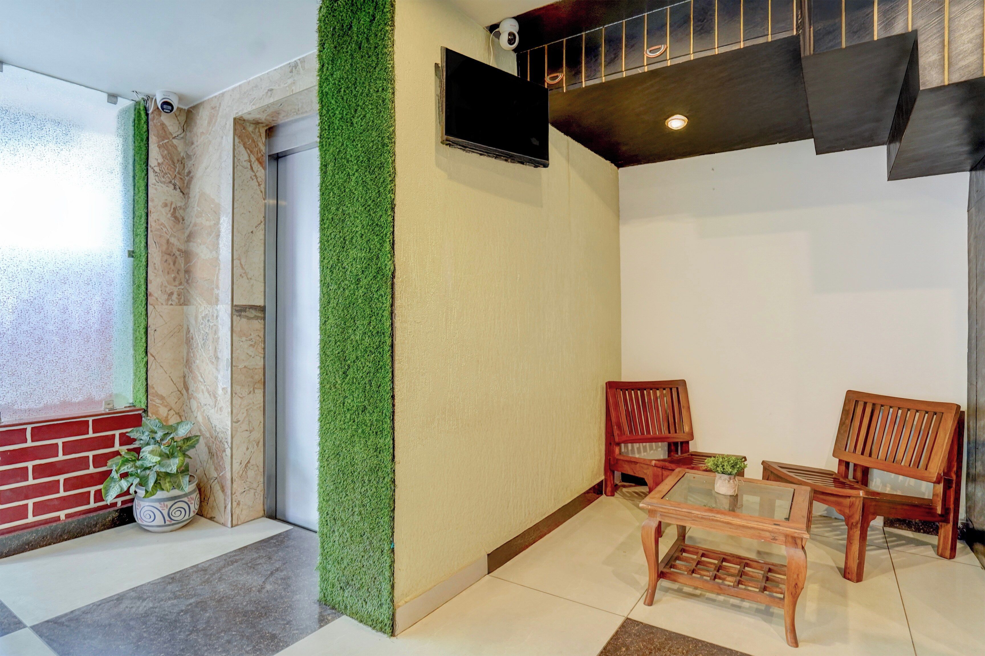 Una habitación con una pared verde, un banco de madera, dos sillas, una mesita y un televisor montado en la pared.