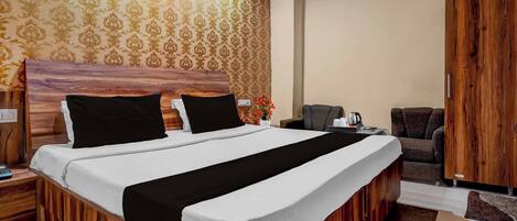 A hotel room with a large bed, a wooden headboard, a nightstand, a desk with a chair, a wardrobe, and a patterned wallpaper.