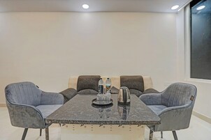A conference room with a rectangular table, four grey upholstered chairs, a water bottle, a glass, and a kettle.