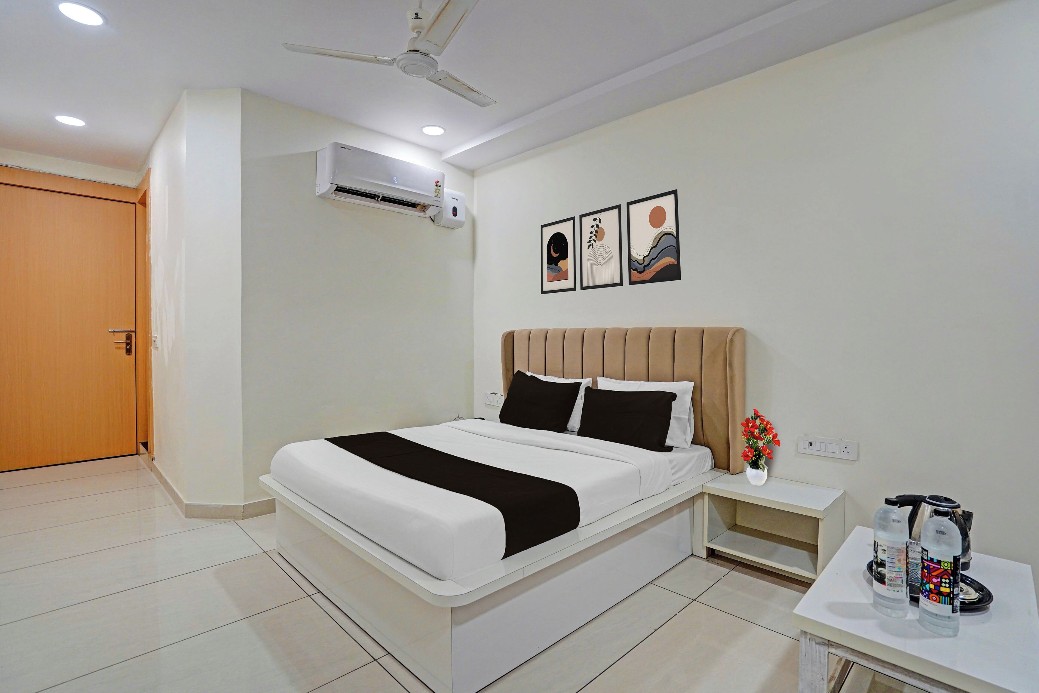 A hotel room with a bed, bedside table, a wall-mounted air conditioner, and a ceiling fan.