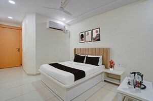 A hotel room with a bed, bedside table, a wall-mounted air conditioner, and a ceiling fan.