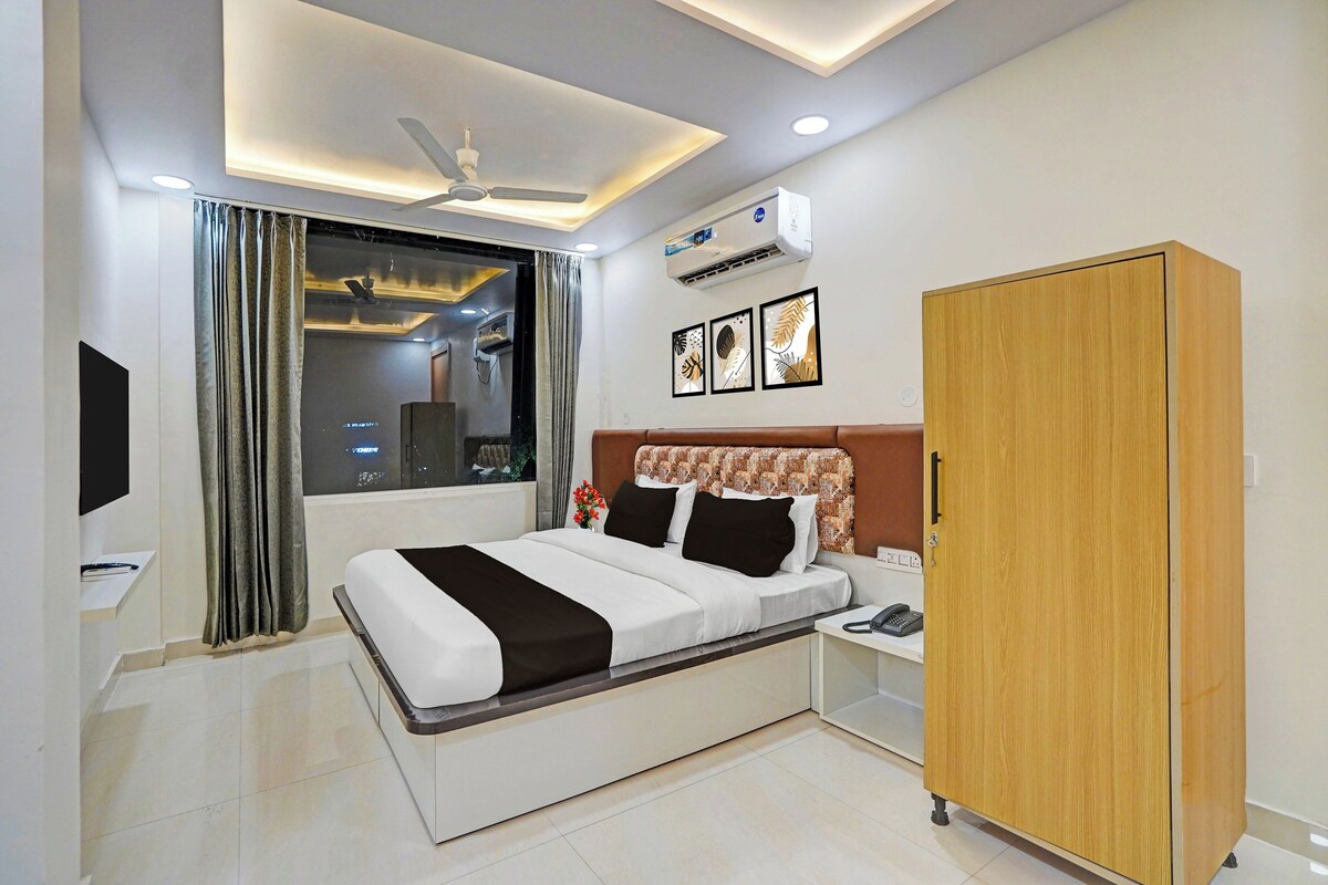 A hotel room with a bed, bedside table, nightstand, wardrobe, and a window with curtains.