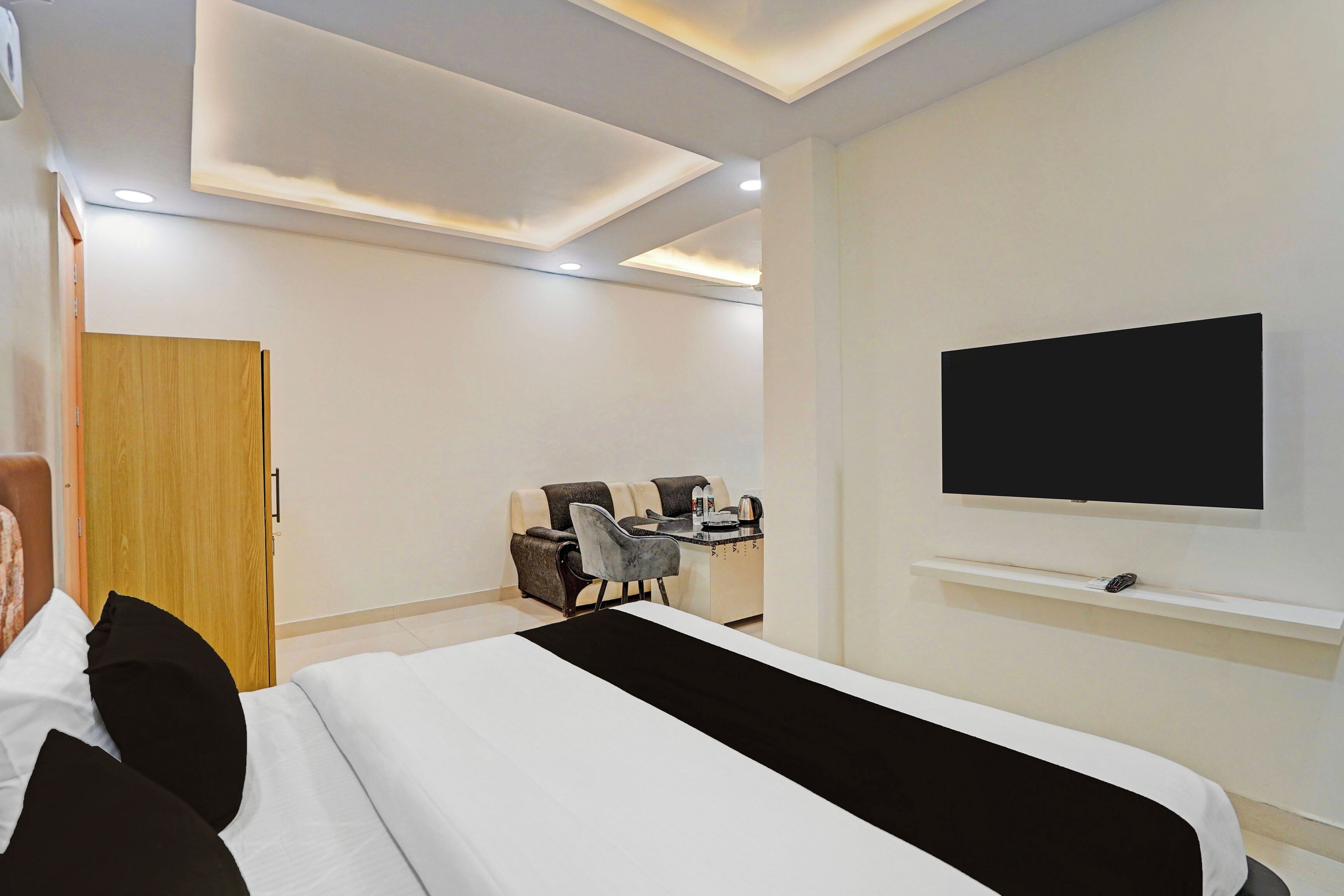 Una habitación de hotel con cama, televisor montado en la pared, escritorio con silla y puerta de madera.