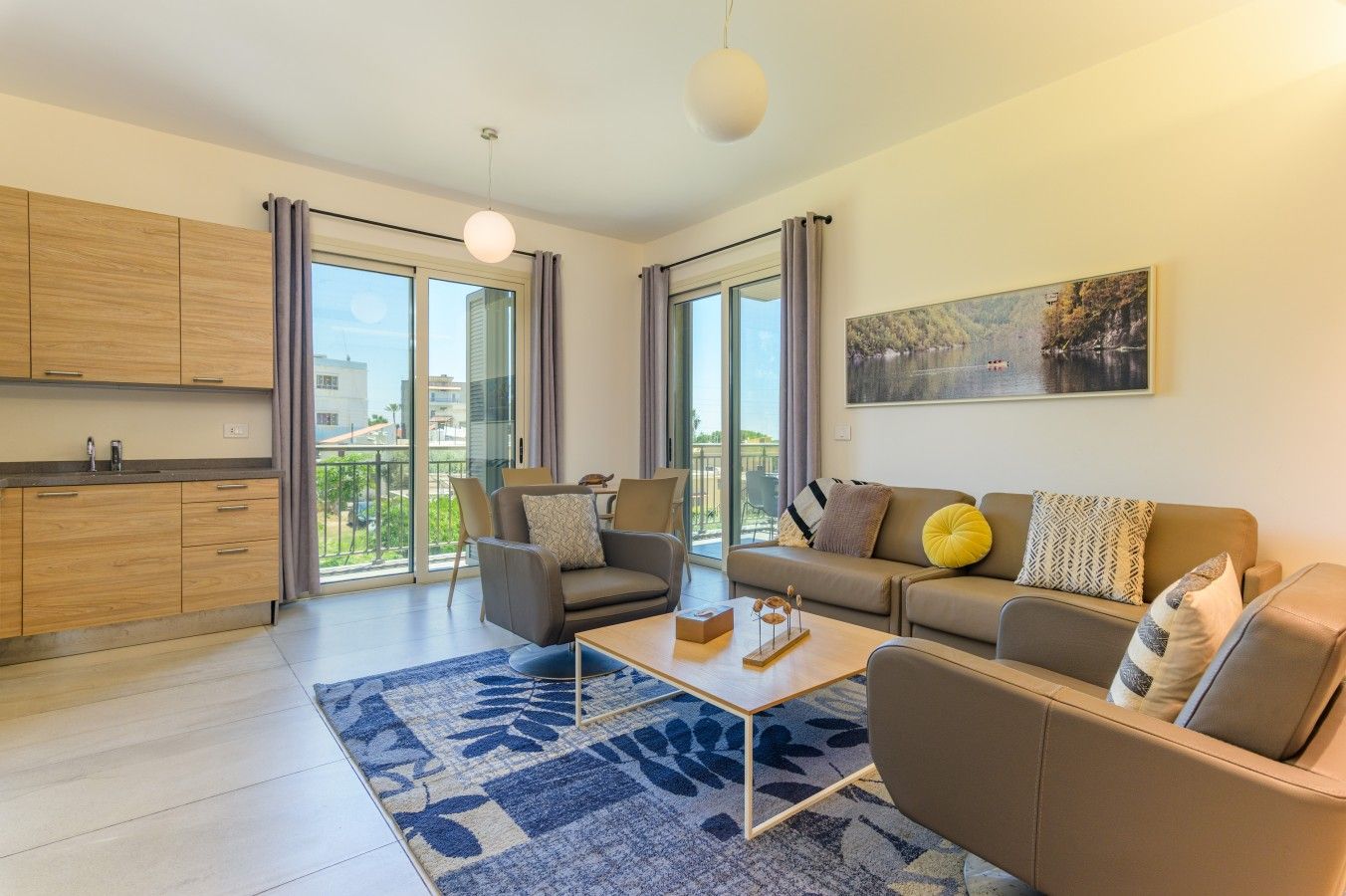 Una sala moderna con un sofá, sillones, una mesa de centro y un amplio ventanal con vistas al exterior.
