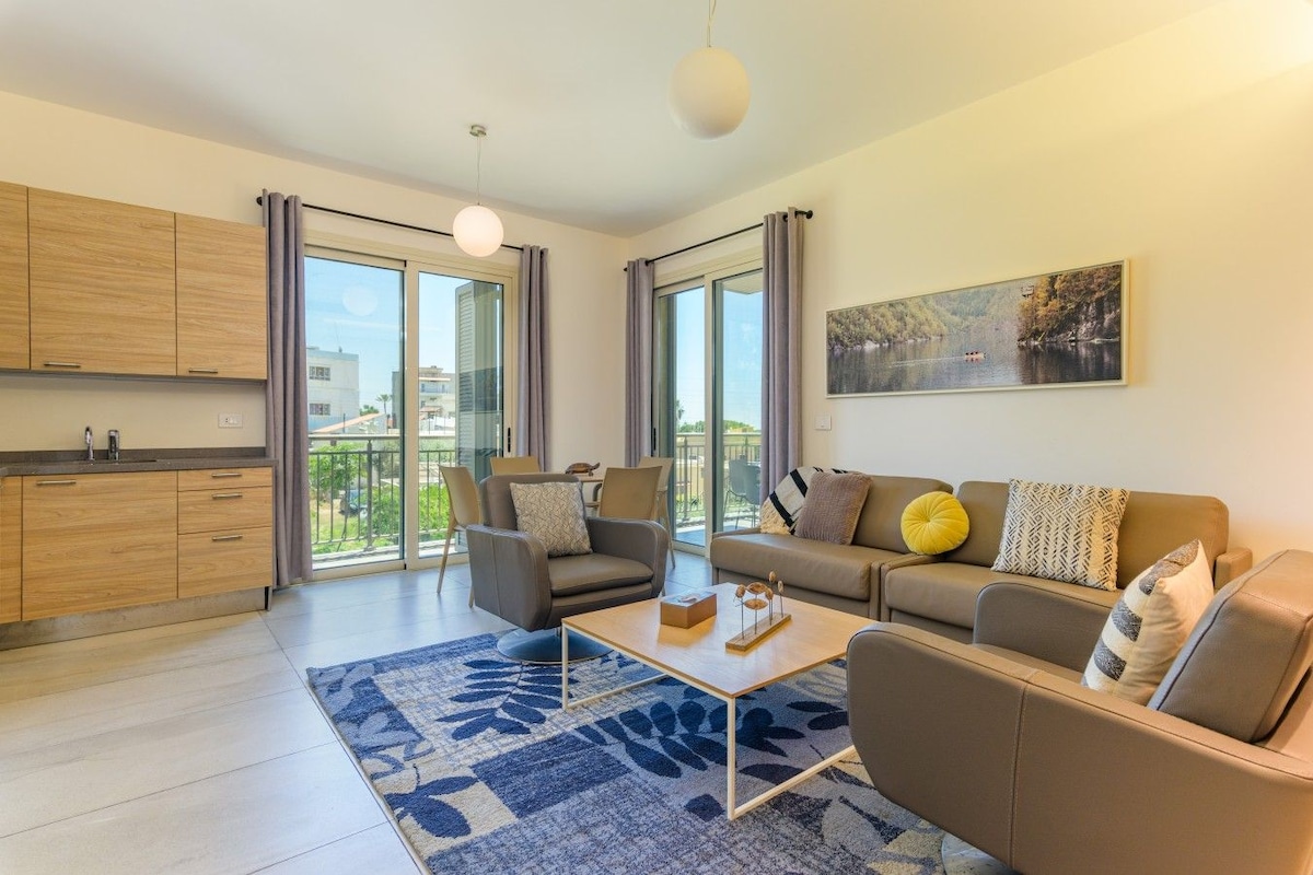 Una sala moderna con un sofá, sillones, una mesa de centro y un amplio ventanal con vistas al exterior.