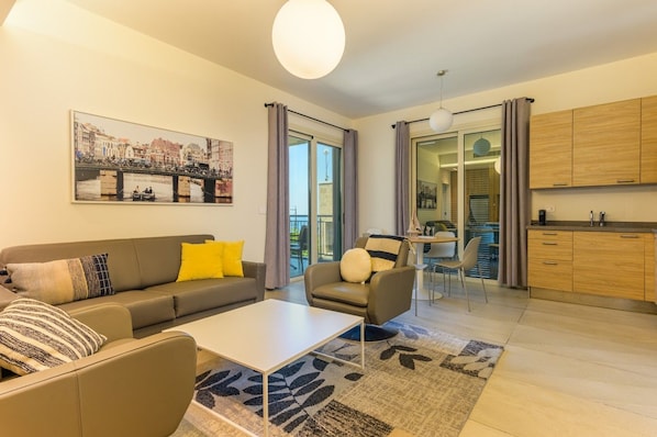 A modern living room with a sofa, armchair, coffee table, and a view of the city through large windows.