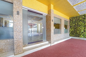 Una entrada de edificio con puerta de vidrio, pared de azulejos y suelo rojo.