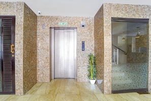 An elevator with a fire lift sign, a potted plant, and a textured glass door. - Townhouse Oak Kozhikode Bus Stand (Kozhikode)