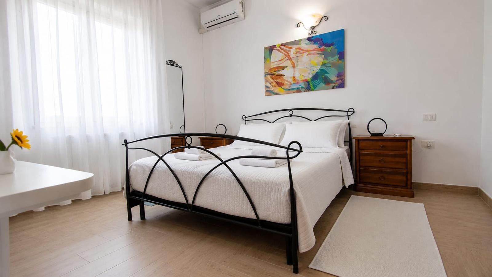 A bedroom with a bed, bedside tables, a dresser, a desk, and a painting on the wall.