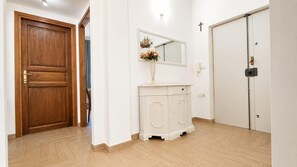 A hallway with a wooden door, a white cabinet with a mirror, and a white door with a cross on the wall.