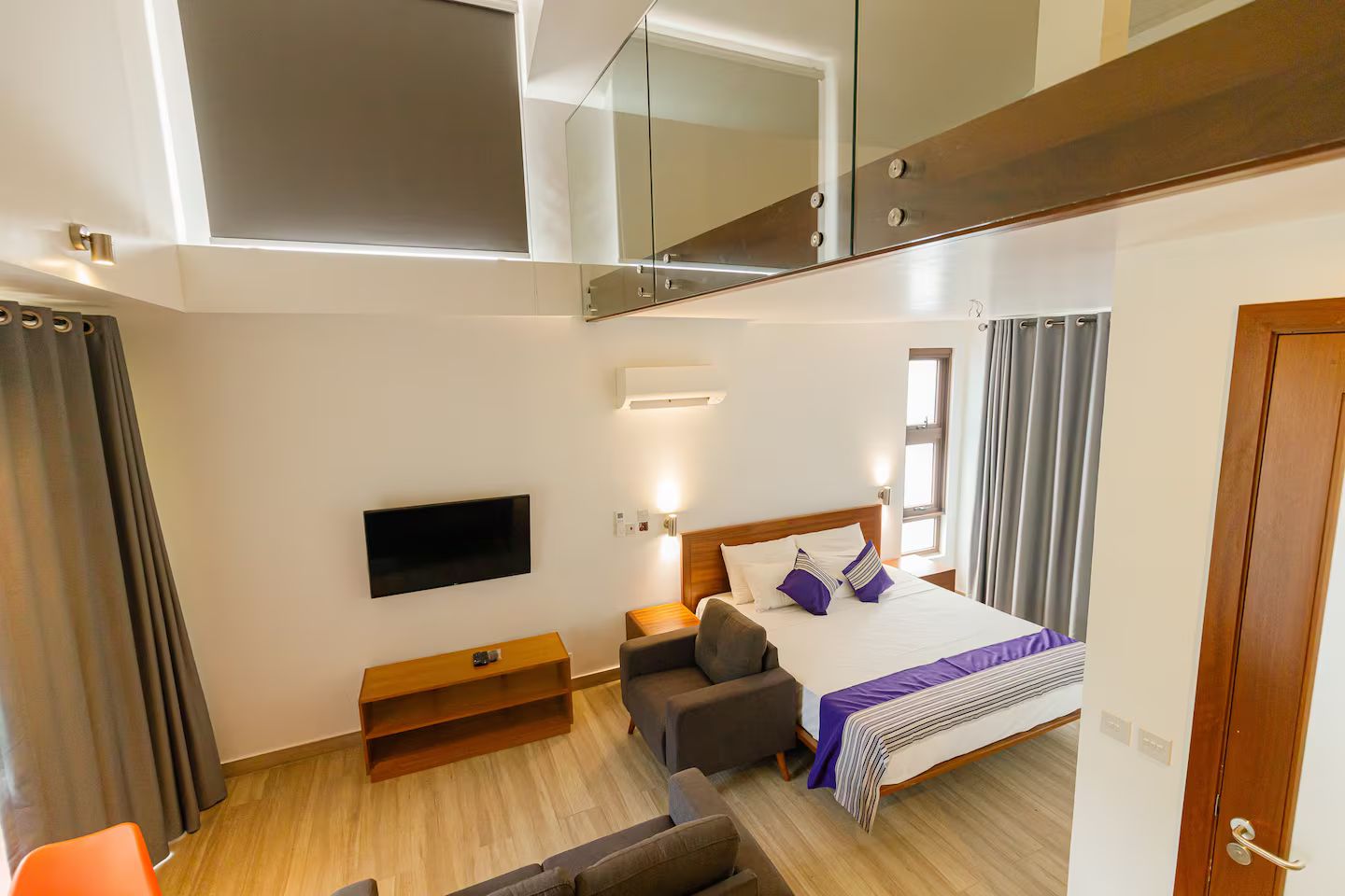 A modern hotel room with a bed, a TV, a seating area, and a balcony.