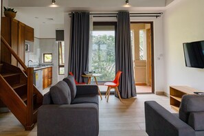 A modern living room with a sofa, a dining area with a table and chairs, a kitchen area, and a TV mounted on the wall. - Garden loft 302 (Adenta Municipality)