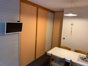 A room with a white table, wooden chairs, a TV mounted on the wall, and a hanging decoration.