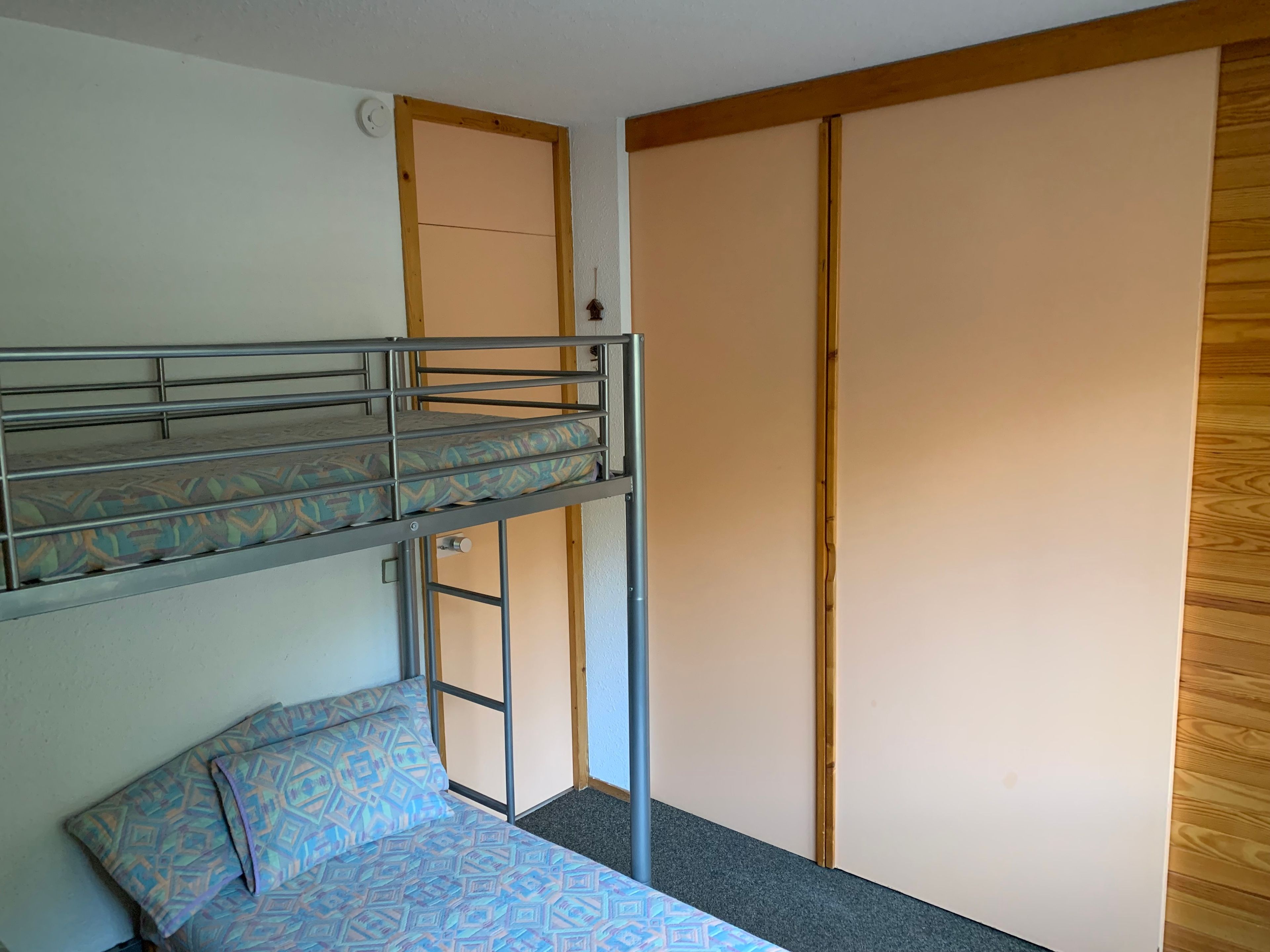 Un lit superposé avec un matelas à motifs, un lit simple avec un oreiller à motifs et une armoire en bois avec une porte coulissante.