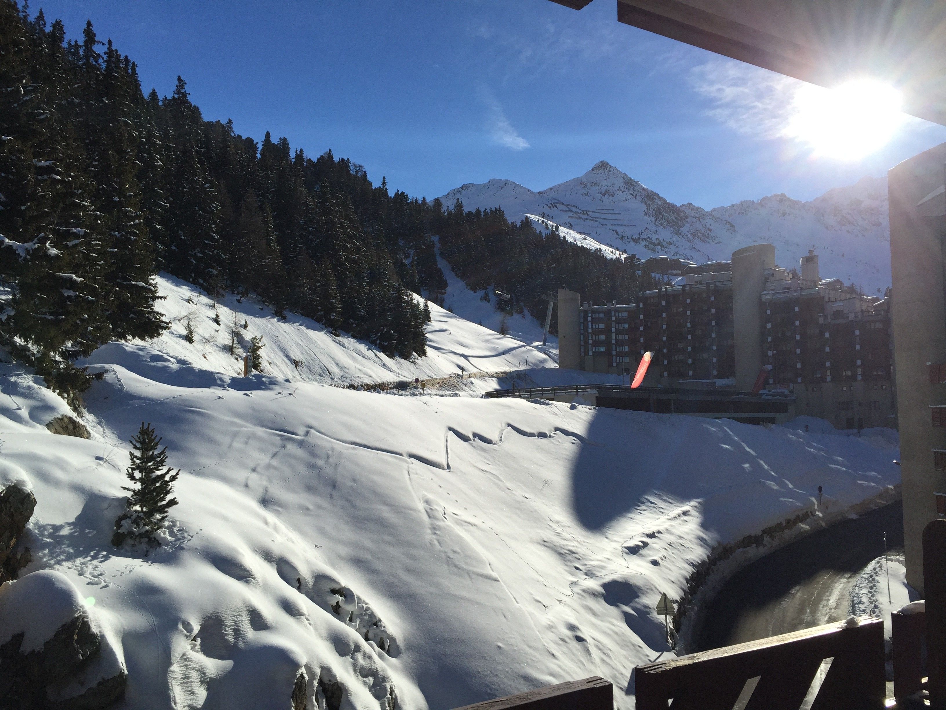 Un paysage de montagne enneigé avec une piste de ski, des bâtiments et un ciel dégagé.