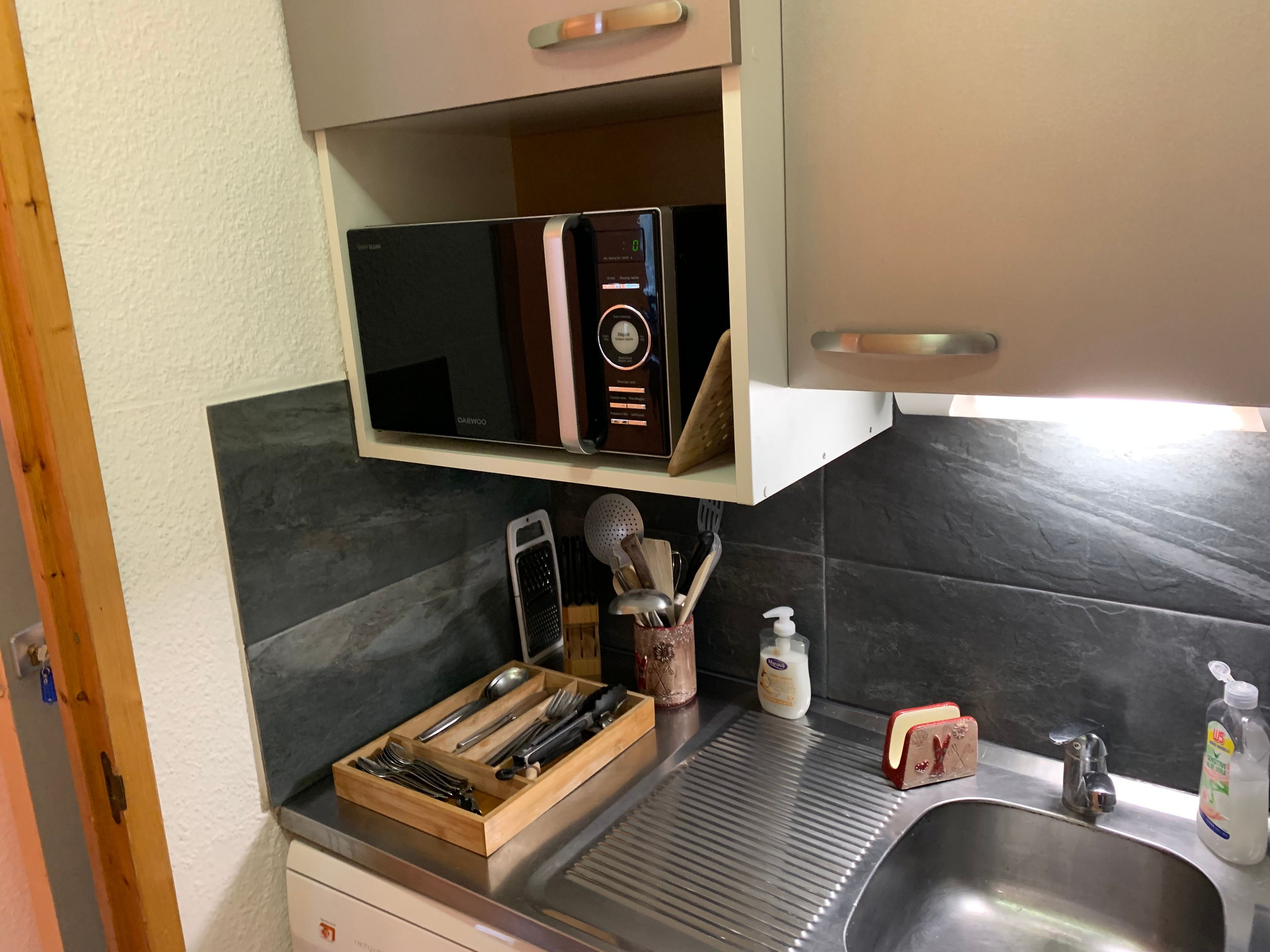 A kitchen with a microwave, a toaster, a sink, and various utensils.