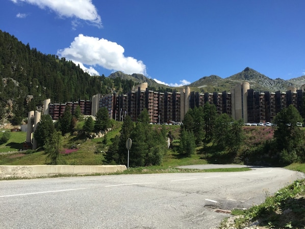 A multi-story hotel with a modern architectural design, situated in a mountainous area with lush greenery and a clear blue sky.
