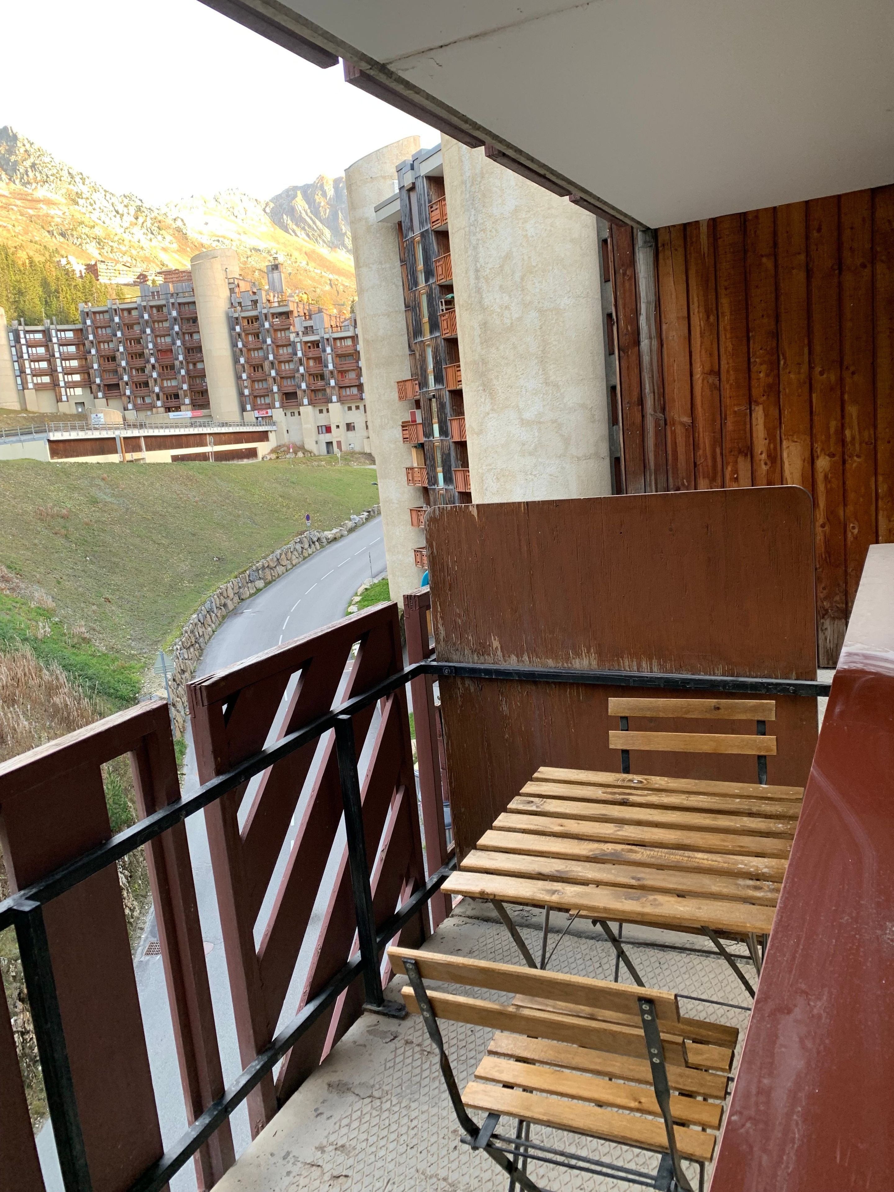 A balcony with a view of a mountainous landscape, a concrete structure with wooden elements, and a metal railing.