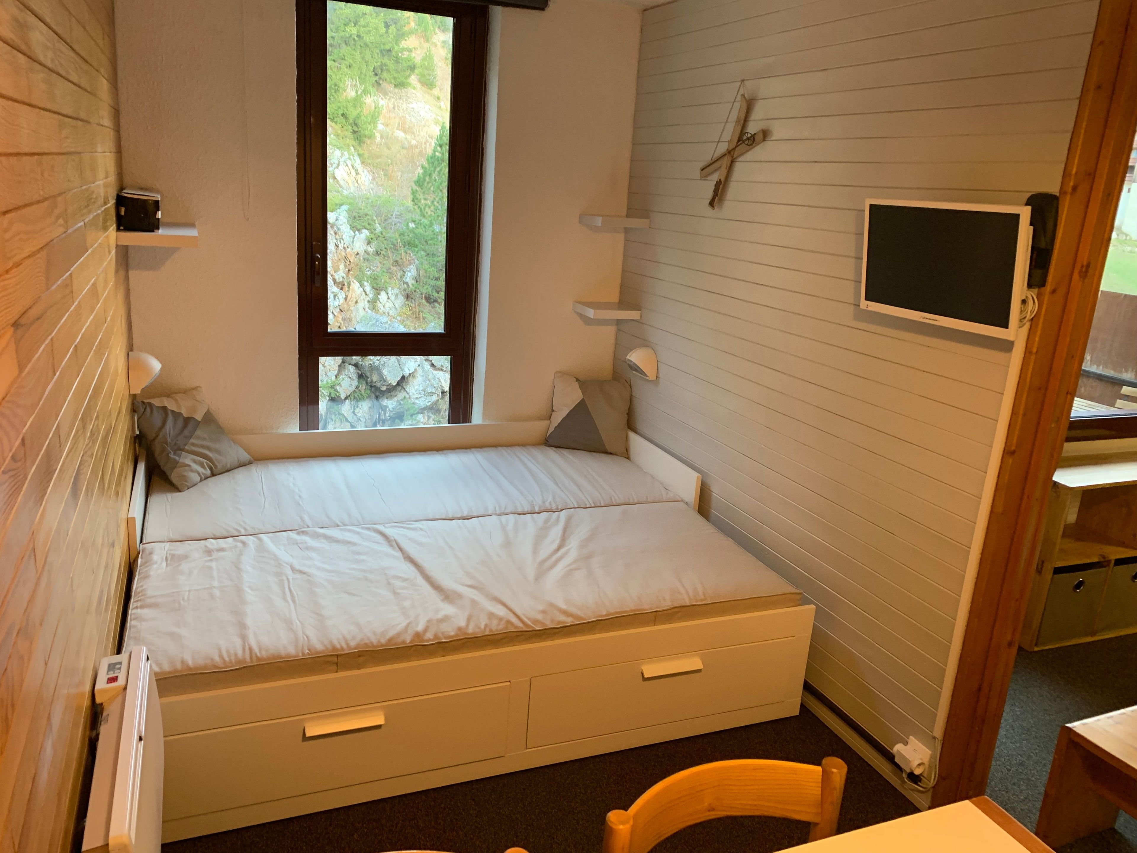 A bedroom with a bed, a window, a TV, and a desk.