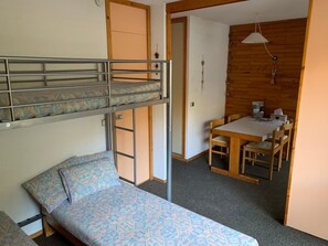 A compact room with bunk beds, a small table, and a chair.