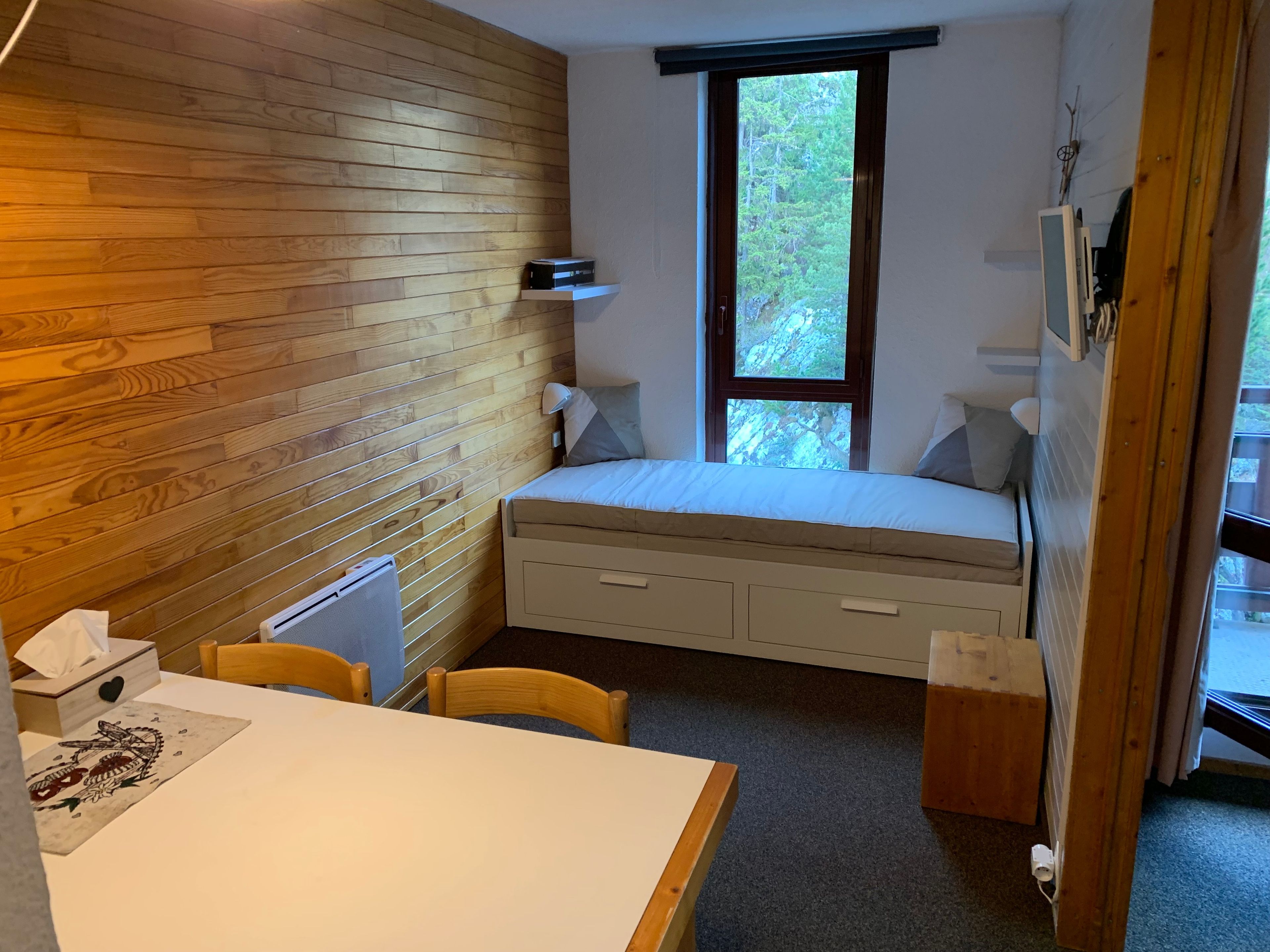 Ein kleines Zimmer mit Bett, Tisch und Fenster.