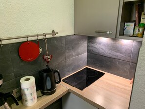 A kitchen with a black induction cooktop, a kettle, and a roll of paper towels on the counter.