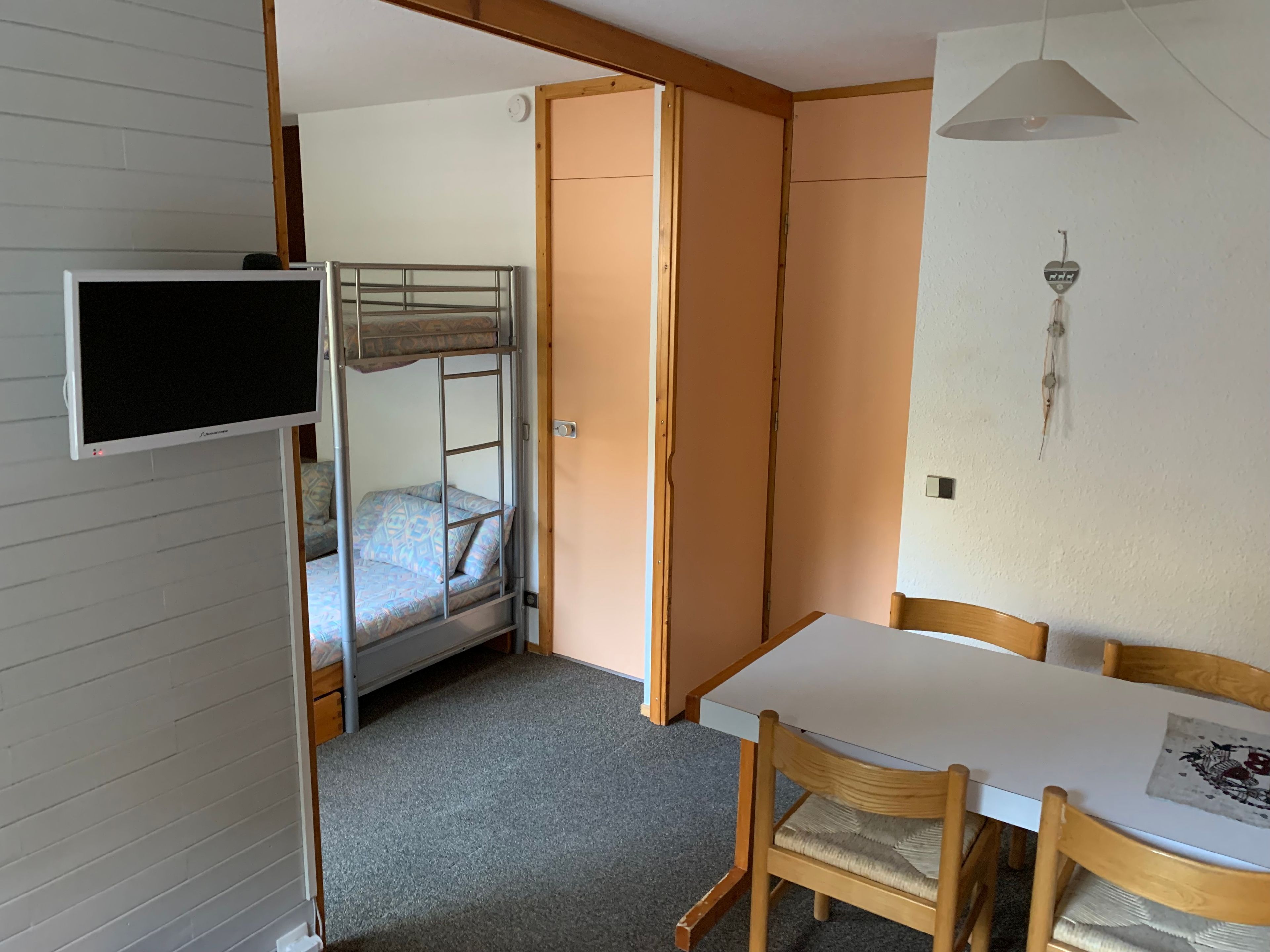 A room with a bunk bed, a desk, a chair, a television, and a wall-mounted light fixture.