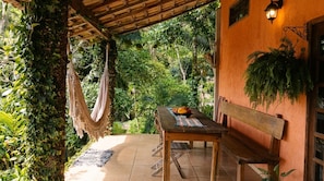 An outdoor patio with a wooden table and bench, surrounded by lush greenery and a hammock. - New Listing (Paraty)
