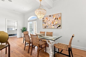 A dining area with a glass table surrounded by wicker chairs, a chandelier, and a large abstract painting on the wall. - Welcome to Soleil House, a  Seacrest Beach retreat perfectly located on 30A. (Seacrest)
