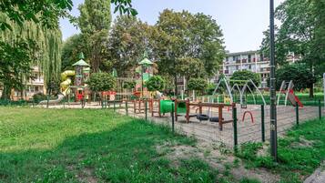 A playground with various play structures, surrounded by grass and trees.
